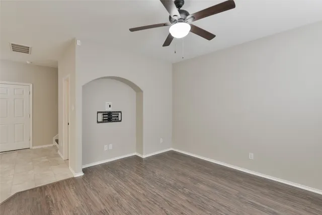 an empty room with wooden floor a ceiling fan and kitchen space with wooden floor
