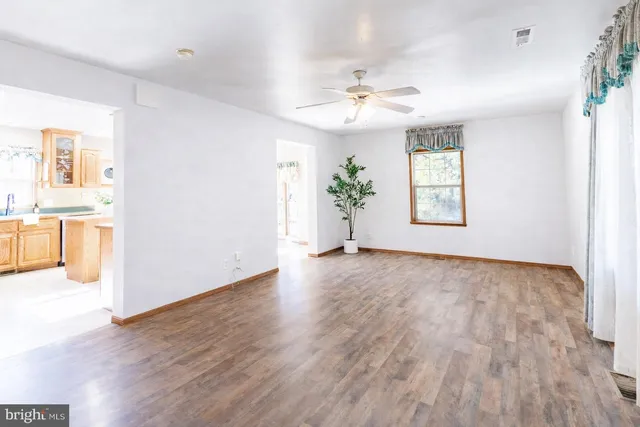 an empty room with wooden floor chandelier fan and windows