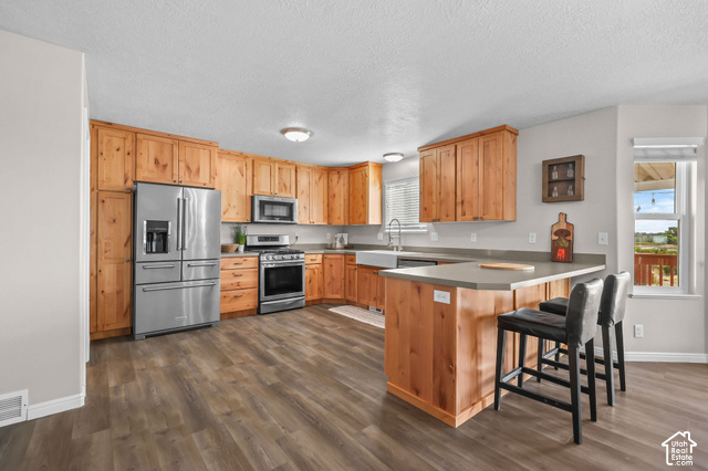 1045 West 3600th South Perry, UT 84302 - Photo 12 of 57 Kitchen featuring wood-finish cabinetry, stainless steel appliances, a farmhouse sink, and an extended countertop island