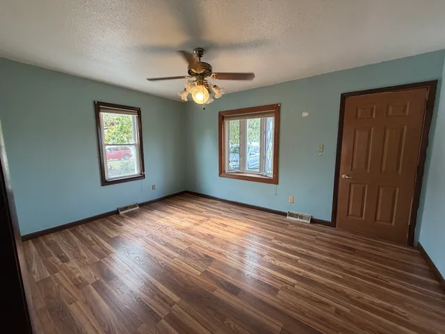 a view of empty room with wooden floor and fan