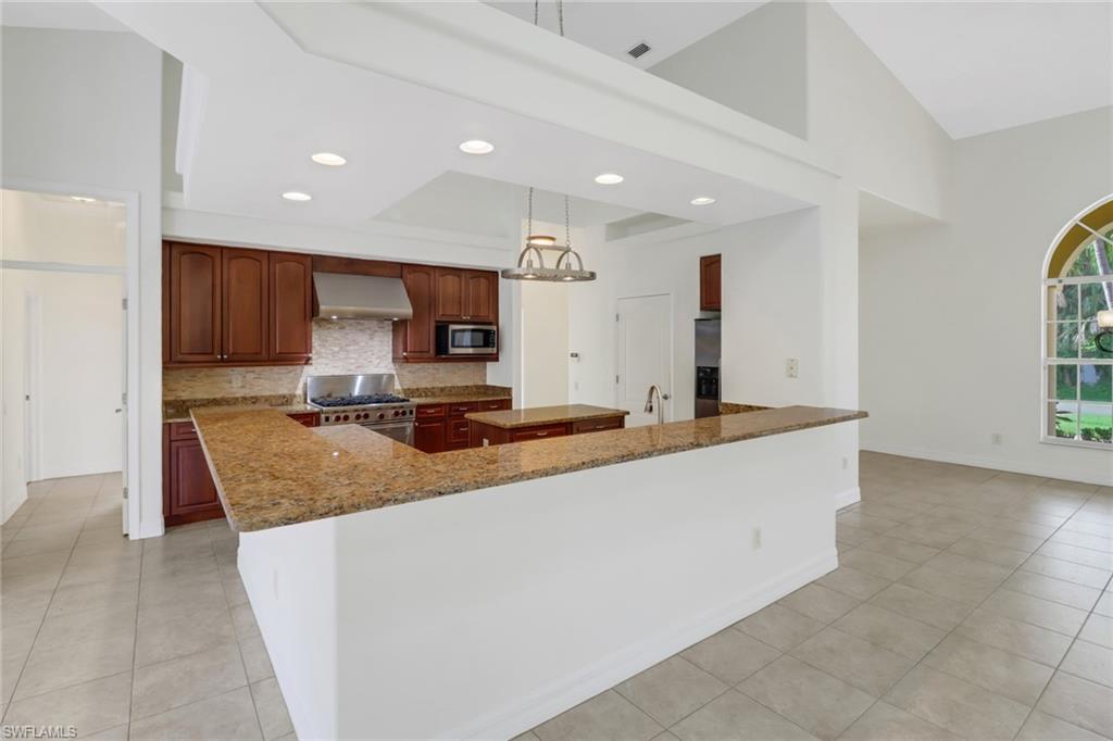 15480 River By Road Fort Myers, FL 33908 - Photo 13 of 48 Kitchen featuring appliances with stainless steel finishes, wall chimney exhaust hood, tasteful backsplash, light tile patterned floors, and dark stone countertops