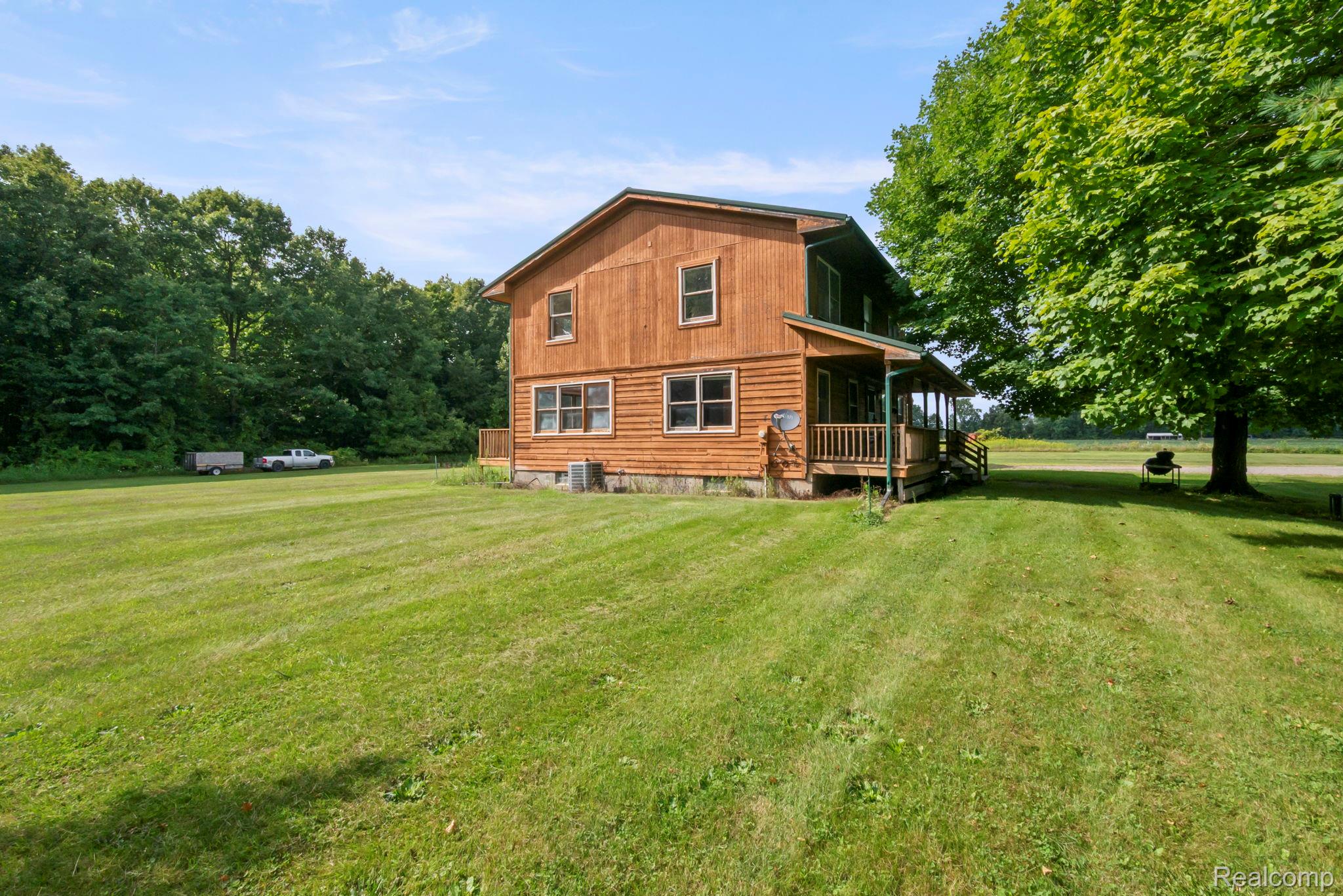 76565 McFadden Road Armada, MI 48005 - Photo 70 of 95 Wood-sided exterior with multiple windows, an inviting covered porch, and a large, verdant lawn