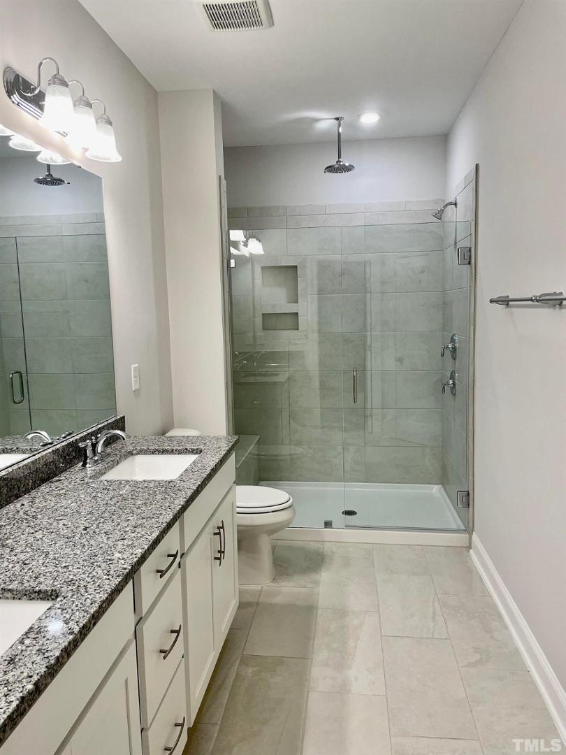 8425 Garnet Rose Drive Raleigh, NC 27615 - Photo 9 of 11 a bathroom with a granite countertop sink a toilet a mirror and shower