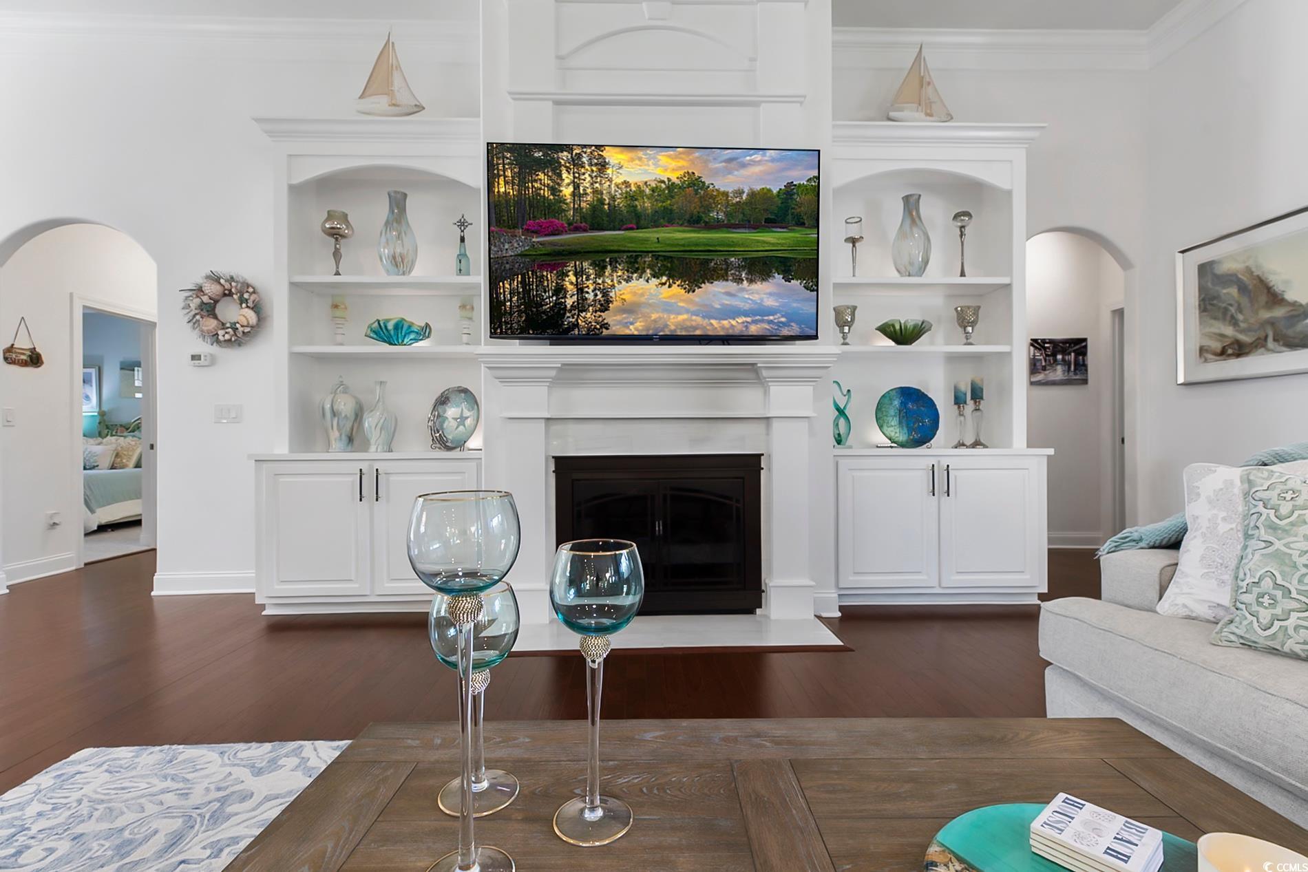 4000 Girvan Drive Myrtle Beach, SC 29579 - Photo 13 of 40 Living room featuring arched walkways, crown molding, dark wood finished floors, a fireplace with flush hearth, and built in shelves