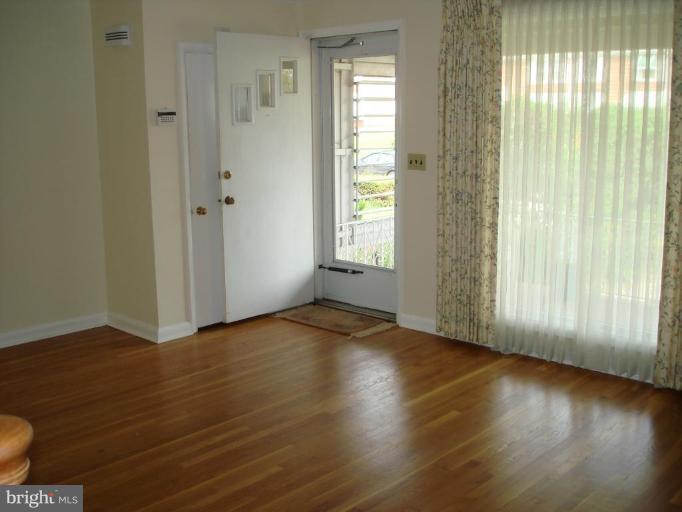6110 Dunroming Road Baltimore, MD 21239 - Photo 2 of 11 an empty room with wooden floor and windows with curtains