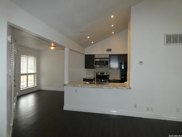 a kitchen with stainless steel appliances a sink a stove a refrigerator a microwave oven with white cabinets and wooden floor