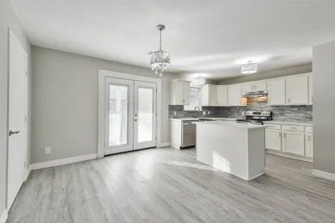 a kitchen with granite countertop a refrigerator a sink dishwasher a stove and white cabinets with wooden floor