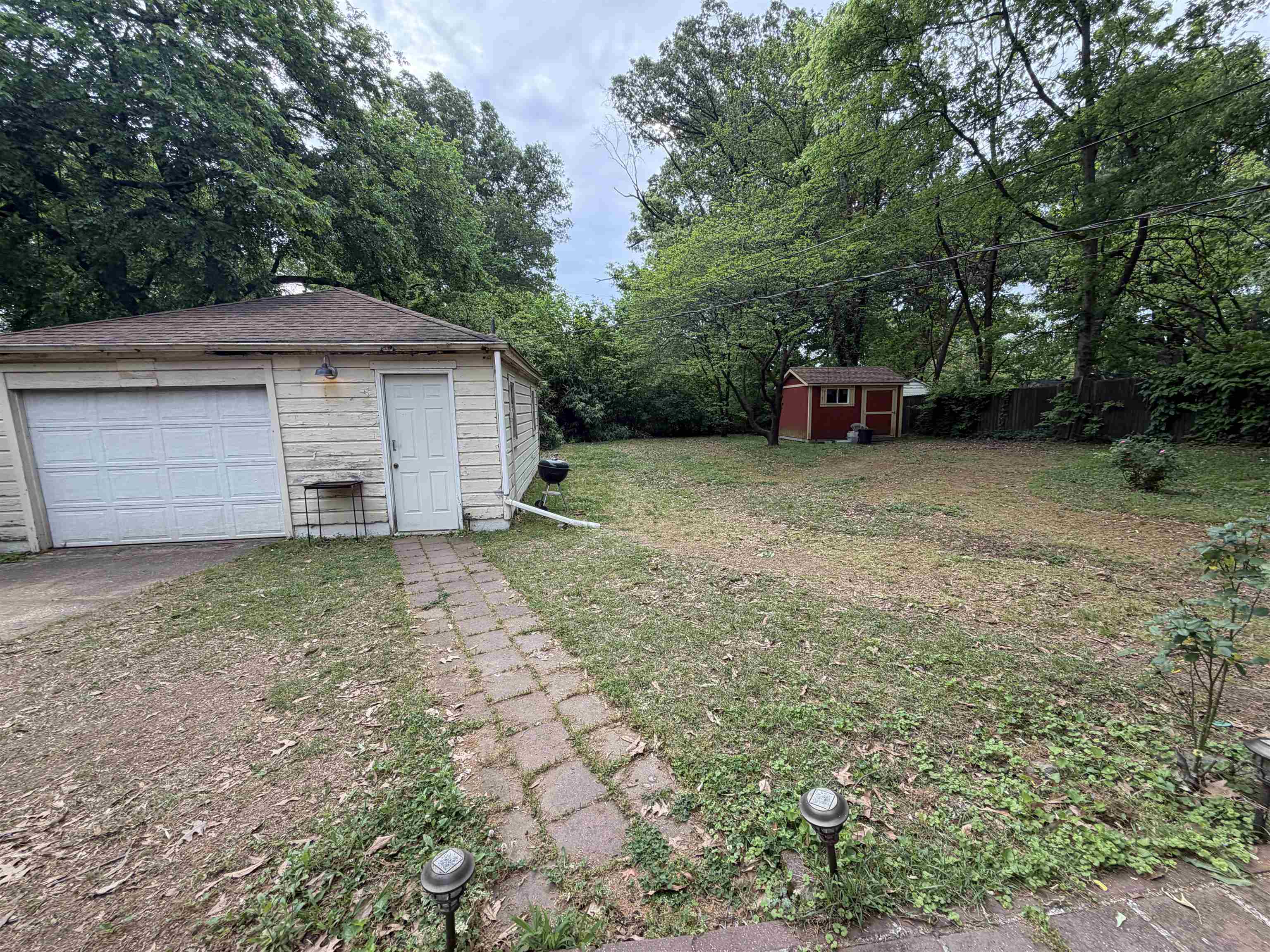 974 Tatum Road Memphis, TN 38122 - Photo 10 of 11 View of green lawn featuring a storage shed, a garage, view of wooded area, and concrete driveway