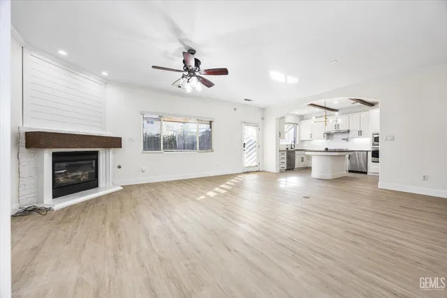 an empty room with wooden floor kitchen view and a fireplace