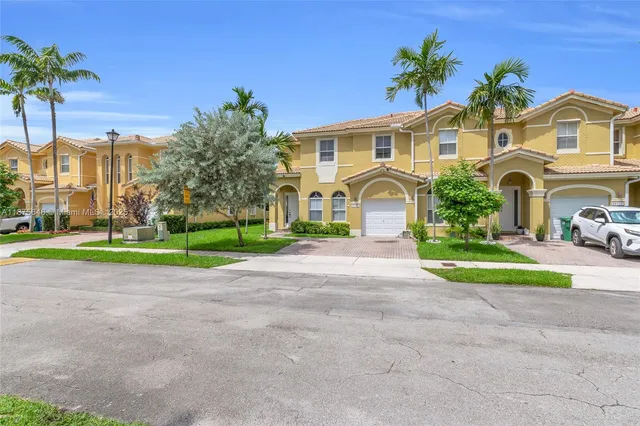 a view of a white house with a big yard and potted plants