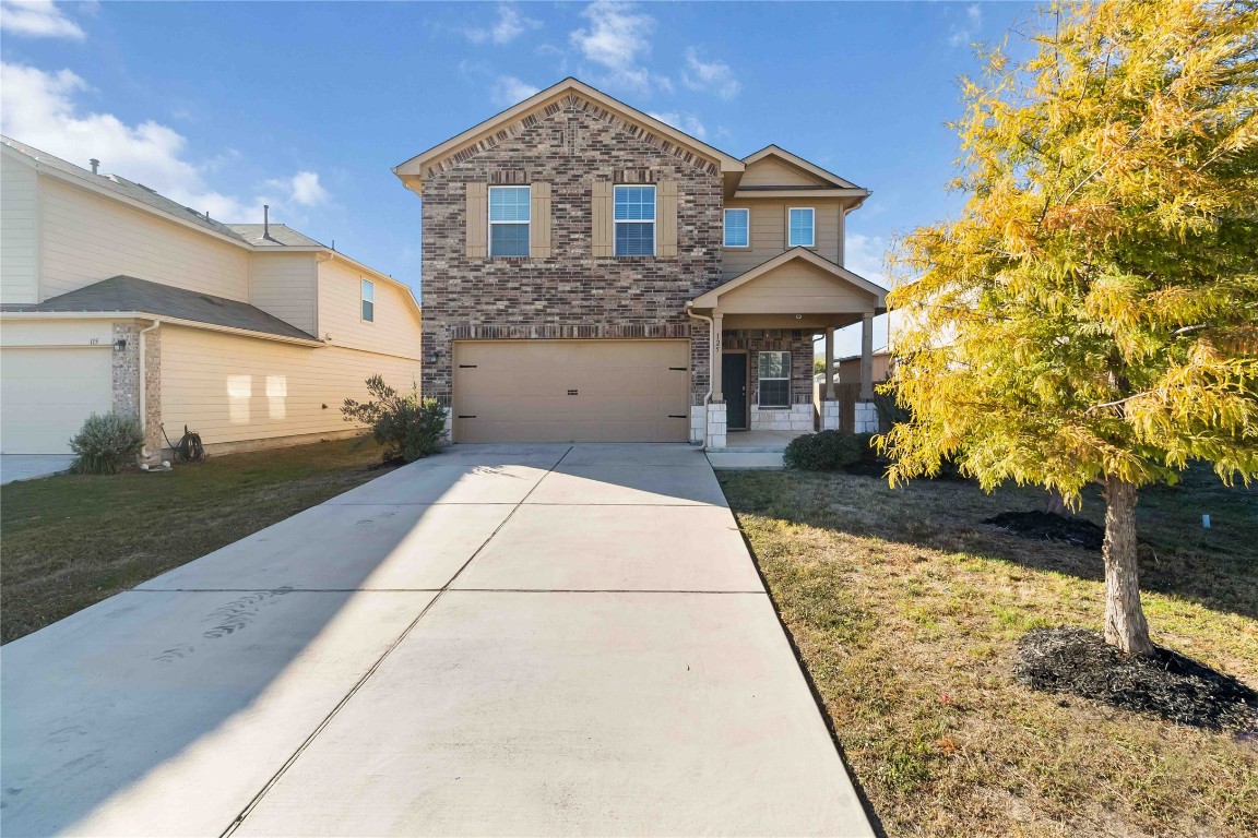 Traditional-style home with brick siding, driveway, an attached garage, and a front lawn