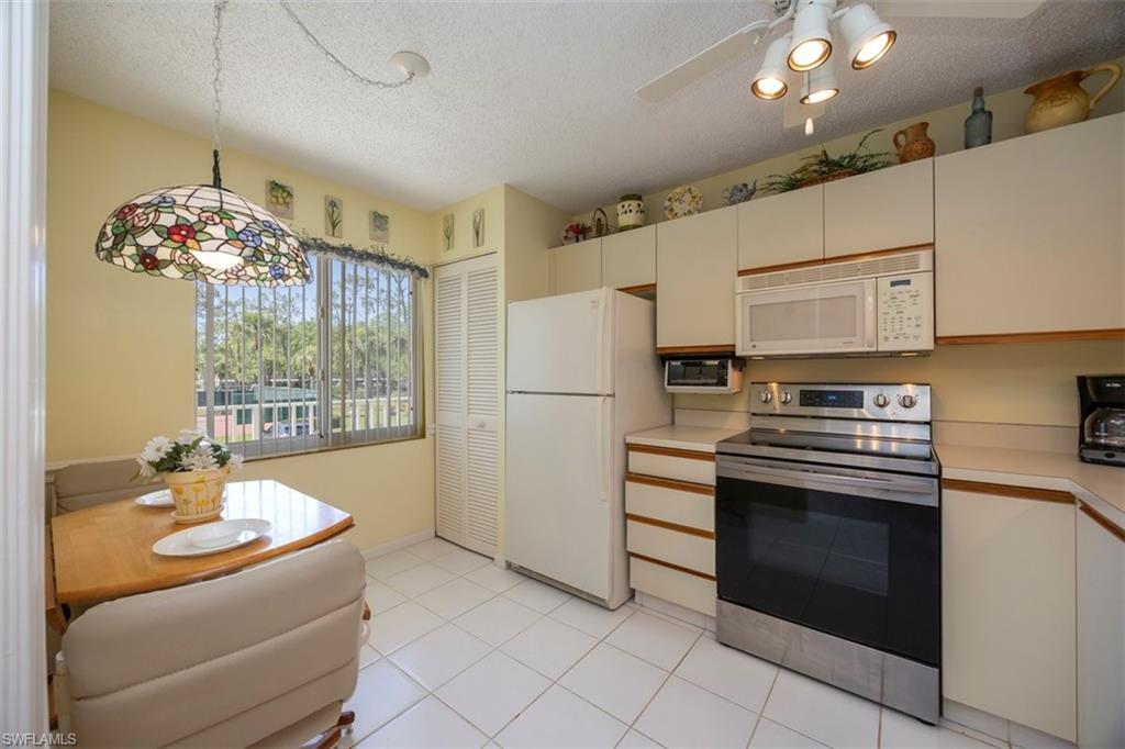 5980 Amherst Drive, Unit D202 Naples, FL 34112 - Photo 4 of 12 Kitchen with light tile patterned flooring, light countertops, a textured ceiling, white appliances, and decorative light fixtures