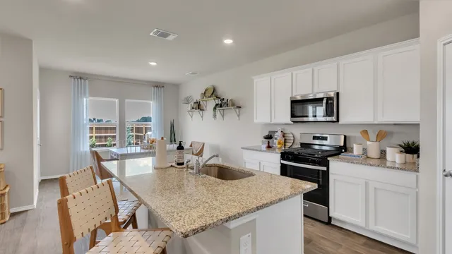a kitchen with kitchen island granite countertop a sink dishwasher stove and white cabinets with wooden floor