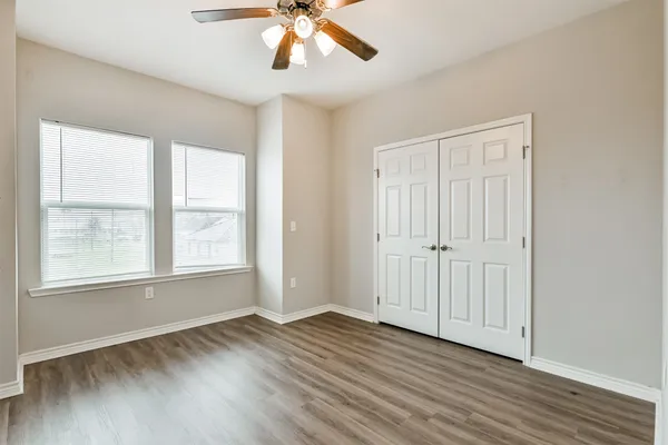 an empty room with wooden floor chandelier fan and windows