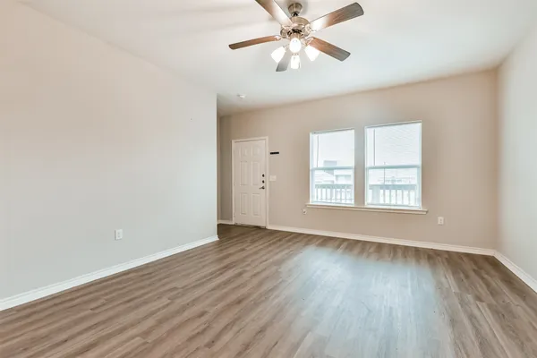 an empty room with wooden floor chandelier fan and windows