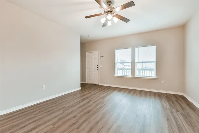 an empty room with wooden floor chandelier fan and windows