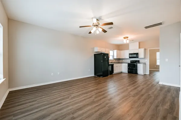 an empty room with wooden floor a ceiling fan a kitchen view and a stove