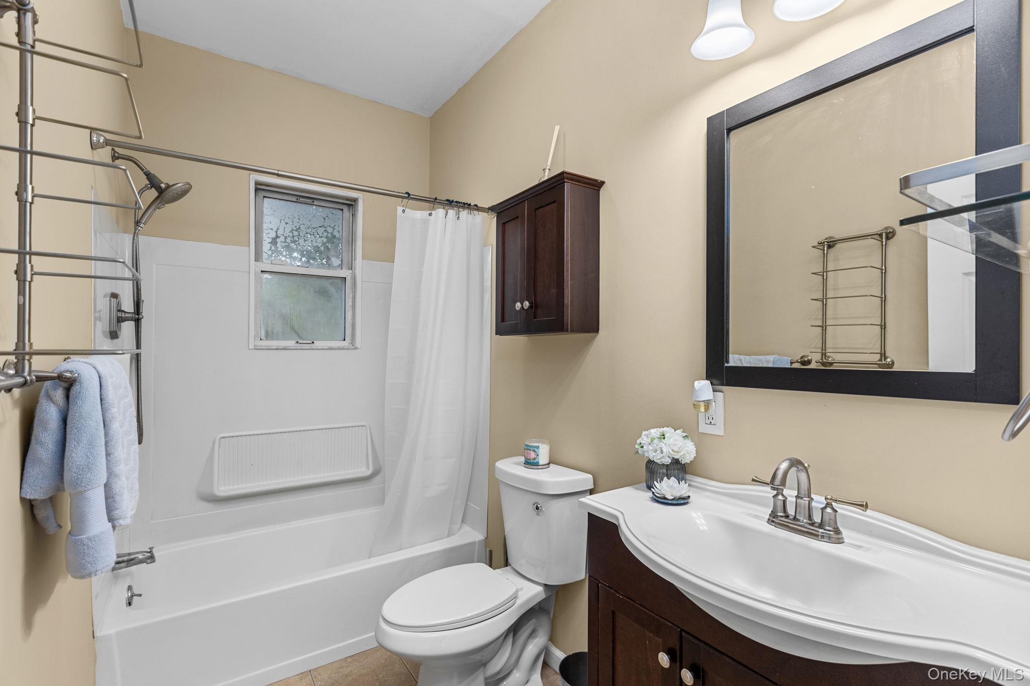 10 Batavia Road Patterson, NY 12563 - Photo 23 of 42 Bathroom featuring a tub/shower combination with a window, a dark wood-finish vanity with an integrated white sink, a matching framed mirror, and a wall-mounted wood-finish cabinet