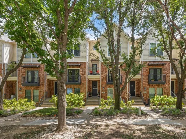 a view of house in front of a yard with plants and large trees