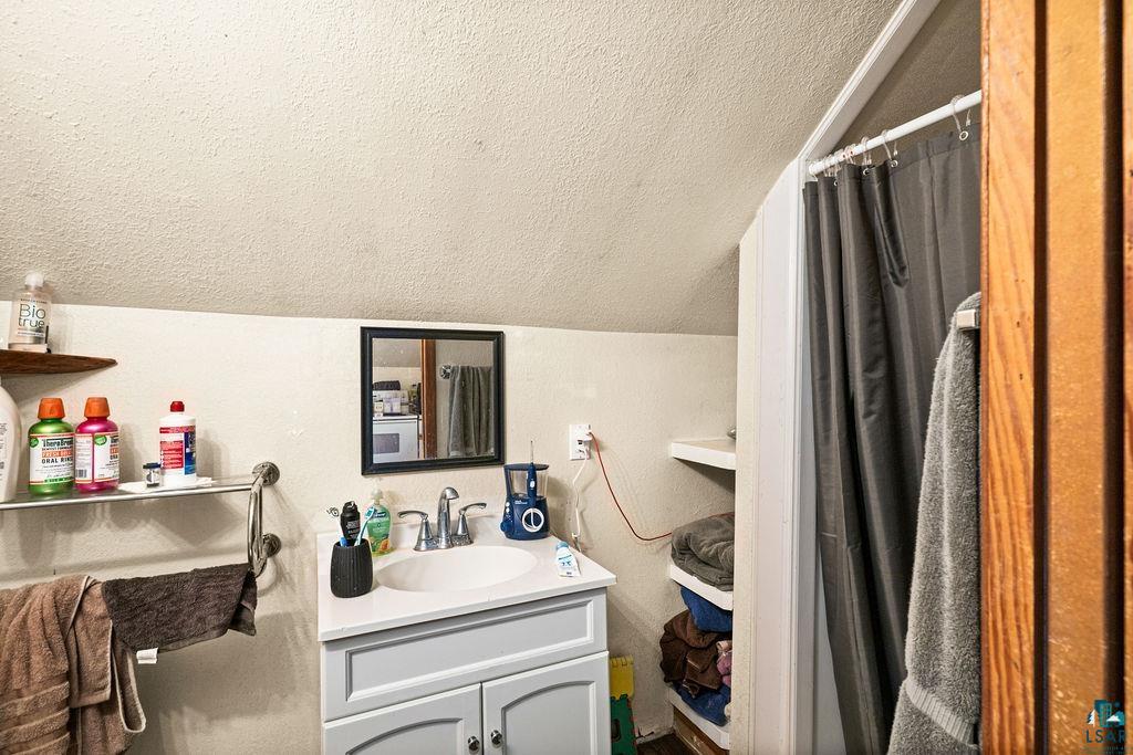 628 West 3rd Street Duluth, MN 55806 - Photo 3 of 8 Full bath featuring a textured ceiling, vanity, a shower with shower curtain, and vaulted ceiling