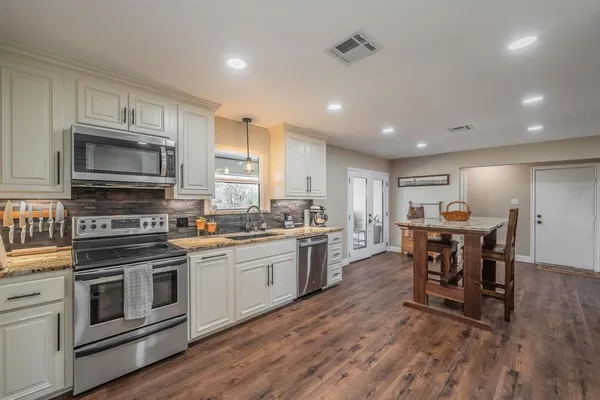 a kitchen with stainless steel appliances granite countertop a stove top oven a sink dishwasher a dining table and chairs with wooden floor