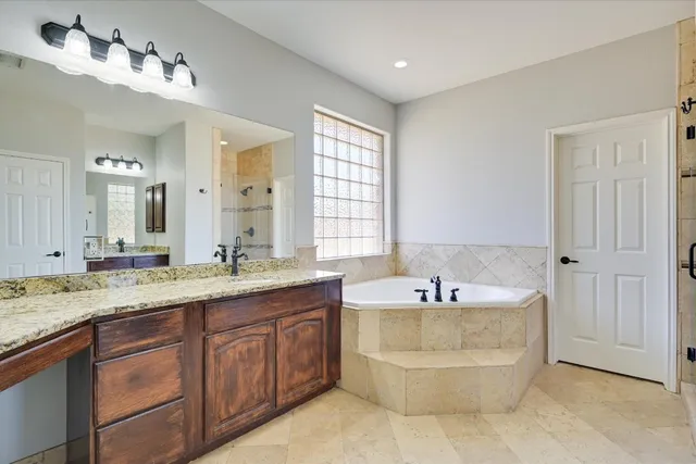 a bathroom with a granite countertop double vanity sink a mirror and a bathtub