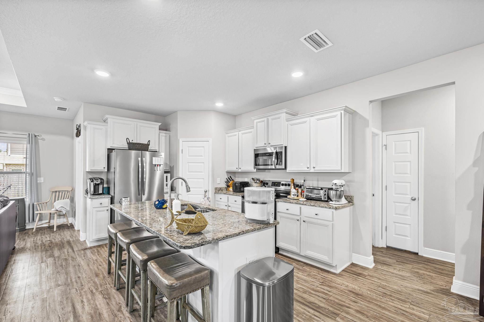 5375 Red Shoulder Road Pace, FL 32571 - Photo 11 of 40 a kitchen with stainless steel appliances a stove a refrigerator a sink dishwasher and a dining table with wooden floor