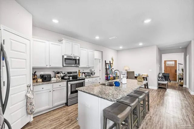 a kitchen with stainless steel appliances kitchen island granite countertop a refrigerator a stove a sink dishwasher and a dining table with wooden floor