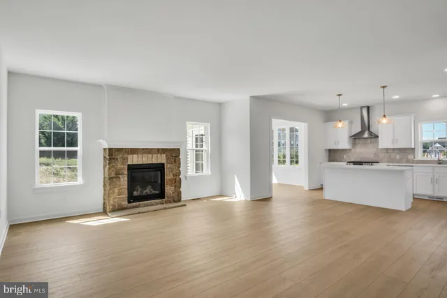 a view of an empty room and kitchen with wooden floor
