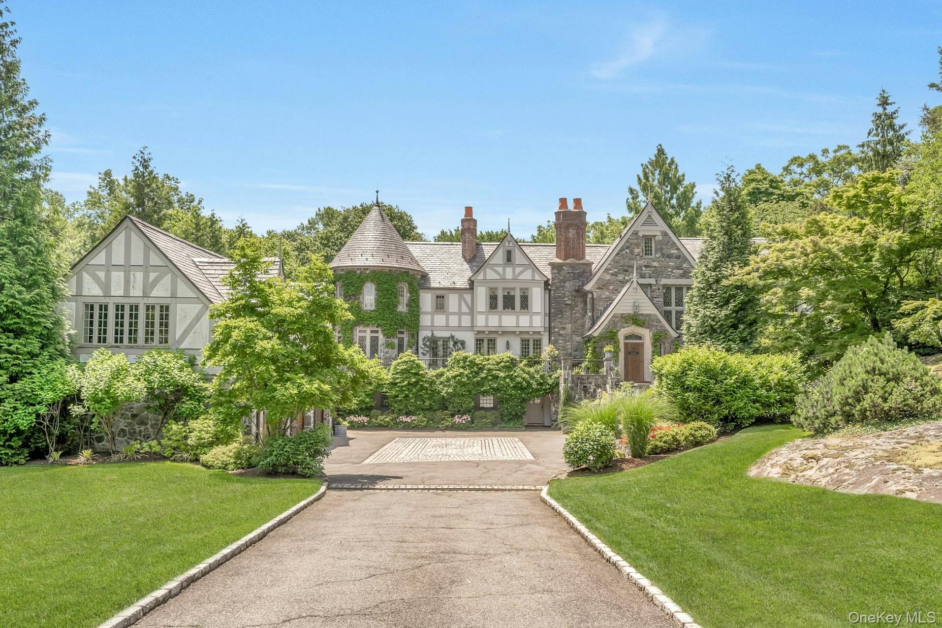 19 Park Drive South Rye, NY 10580 - Photo 1 of 42 Elegant Tudor-style estate set on beautifully landscaped grounds featuring stone and half-timber architecture, a charming ivy-covered turret, and stately chimneys. The driveway leads to a grand entrance, surrounded by manicured lawns, mature trees, and lush gardens, creating a private and timeless retreat.