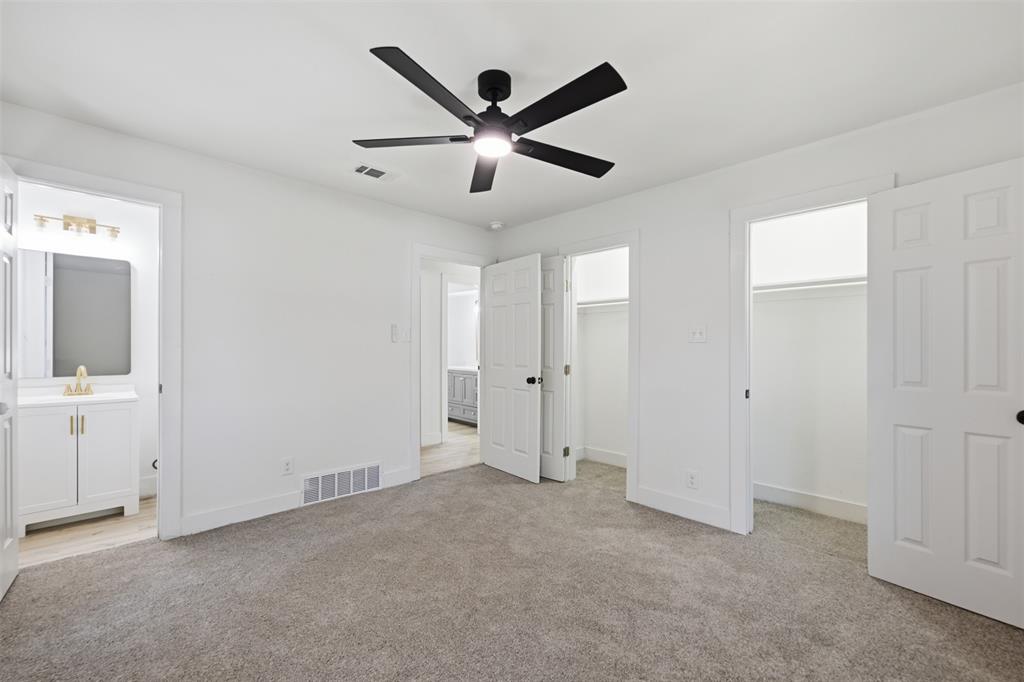 3308 Rufus Street Fort Worth, TX 76119 - Photo 12 of 17 Carpeted room featuring a matte black ceiling fan, two closet openings with hanging rods, and a white interior door leading to a bathroom with a vanity, mirror, and light fixture