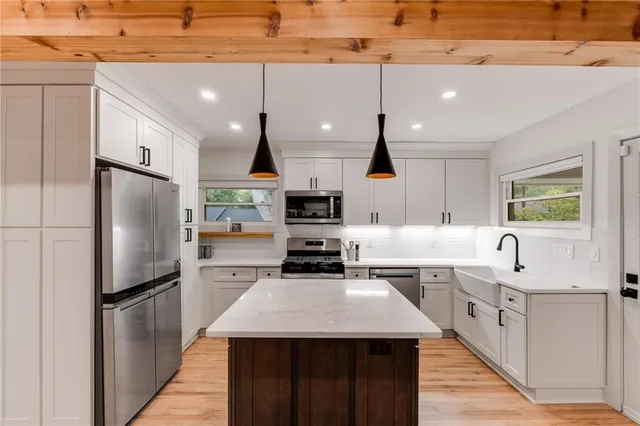 a kitchen with stainless steel appliances kitchen island granite countertop a refrigerator a sink dishwasher a oven with white cabinets and wooden floor
