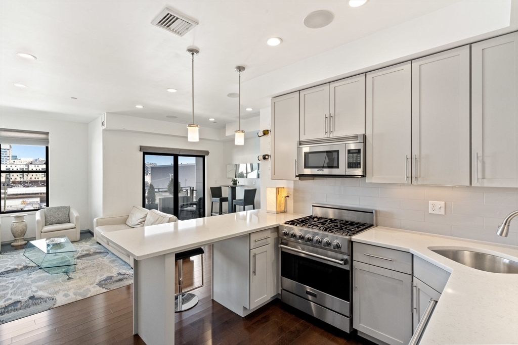 345 D Street, Unit 11 Boston, MA 02127 - Photo 12 of 23 a kitchen with stainless steel appliances white cabinets a sink a stove a microwave and wooden floors