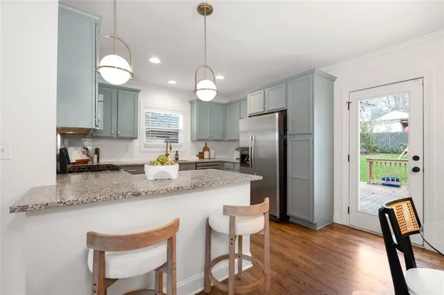 a kitchen with stainless steel appliances granite countertop a refrigerator a sink a stove a dining table and chairs with wooden floor