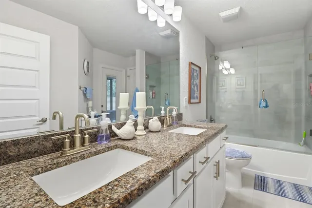 a bathroom with a granite countertop double vanity sink and mirror with shower