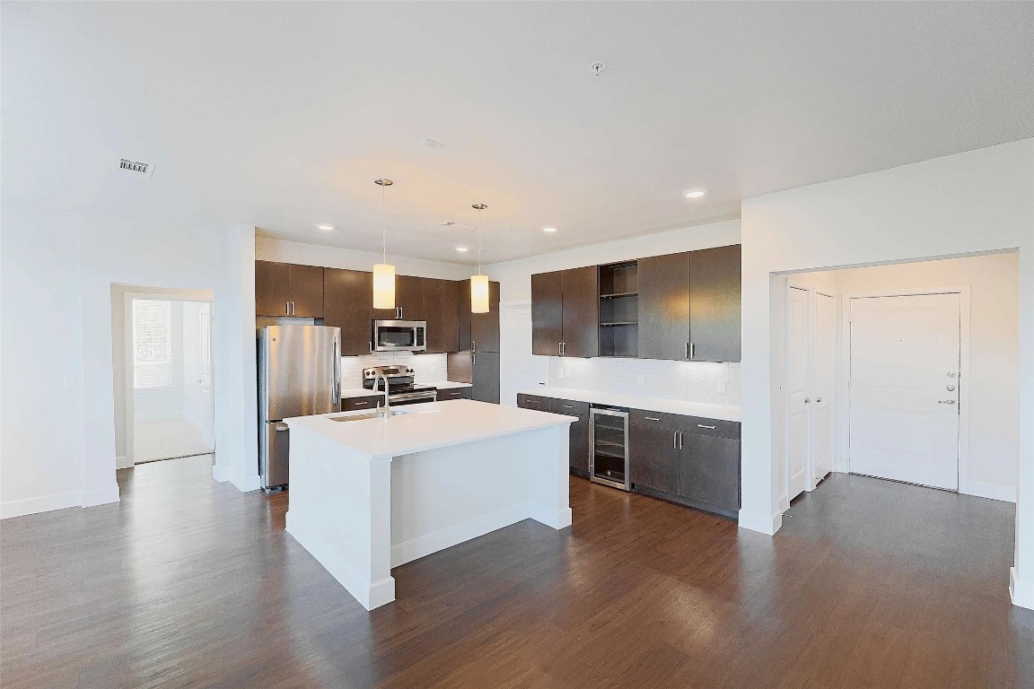 4800 Steiner Ranch Boulevard, Unit 20002 Austin, TX 78732 - Photo 11 of 29 Kitchen featuring dark brown cabinetry, stainless steel appliances, an island with sink, dark wood-style flooring, and recessed lighting