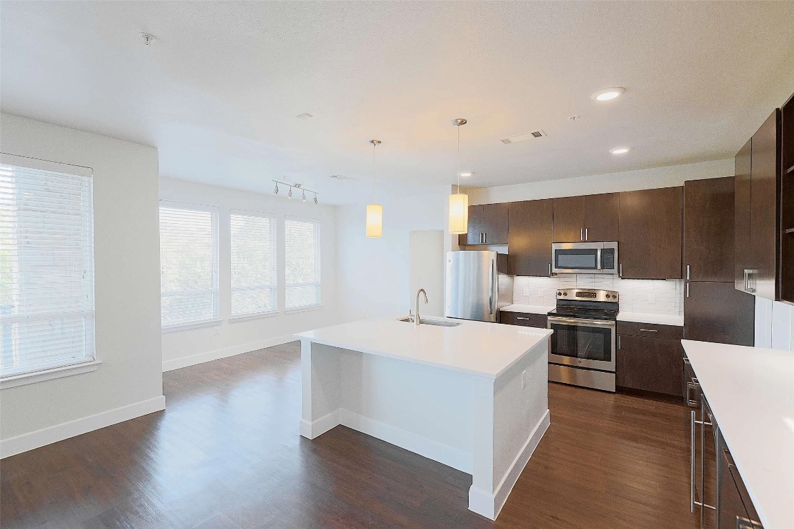 4800 Steiner Ranch Boulevard, Unit 20002 Austin, TX 78732 - Photo 12 of 29 Kitchen with dark brown cabinetry, appliances with stainless steel finishes, pendant lighting, a center island with sink, and dark wood-type flooring