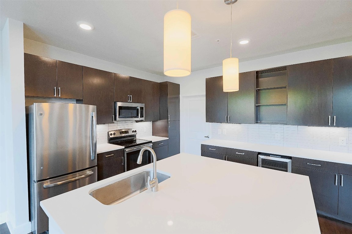4800 Steiner Ranch Boulevard, Unit 20002 Austin, TX 78732 - Photo 13 of 29 Kitchen featuring stainless steel appliances, pendant lighting, open shelves, tasteful backsplash, and dark brown cabinets