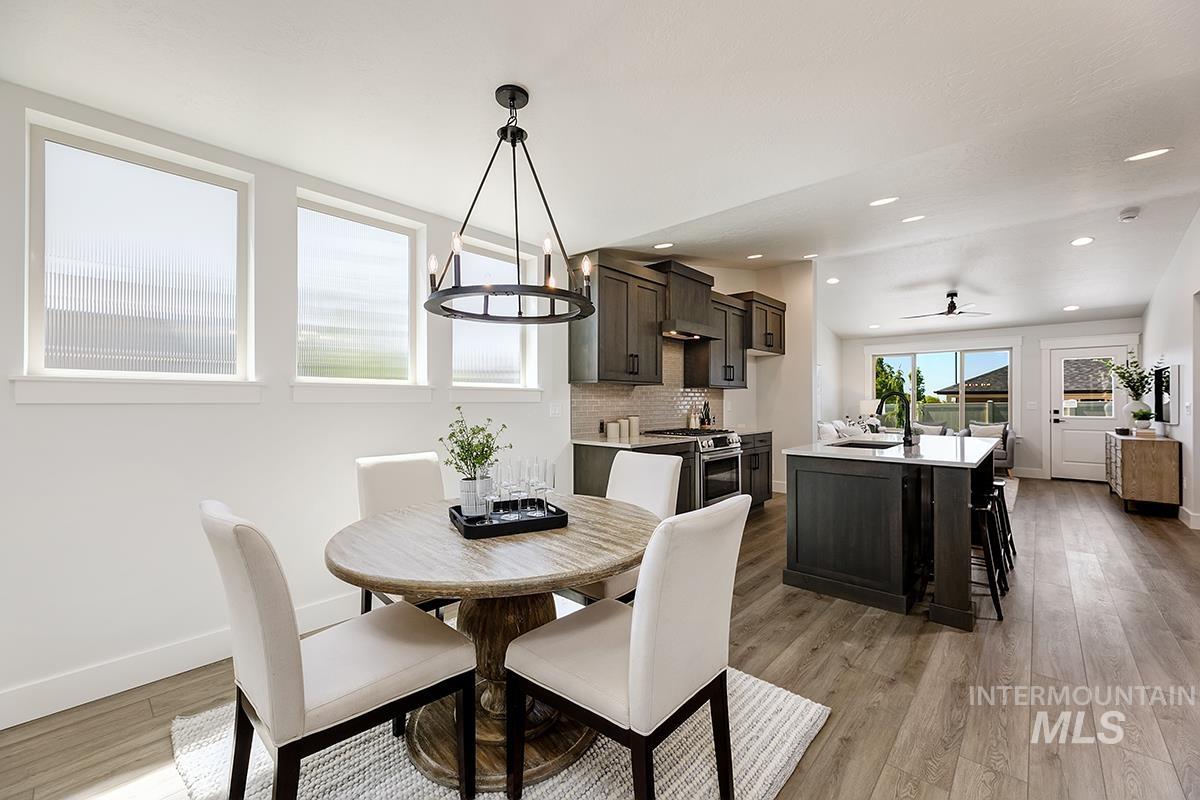 7151 South Skybreak Lane Meridian, ID 83642 - Photo 4 of 26 Open-concept dining and kitchen area featuring wood-finish flooring, a round pedestal dining table, a kitchen island with a light-toned countertop, dark wood-finish cabinetry, and stainless steel appliances