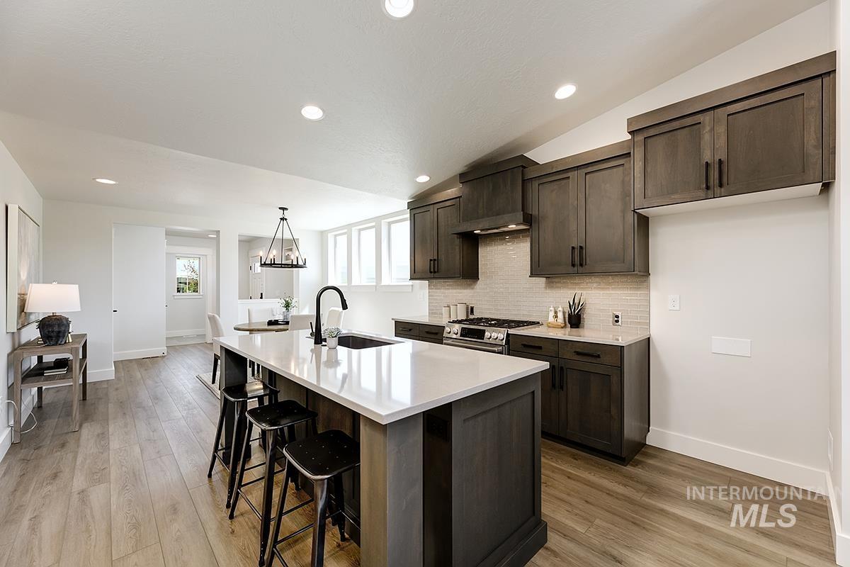 7151 South Skybreak Lane Meridian, ID 83642 - Photo 5 of 26 Kitchen featuring a central island with a white countertop and integrated sink, dark wood-finish cabinetry, a tile backsplash, recessed lighting, and wood-finish flooring