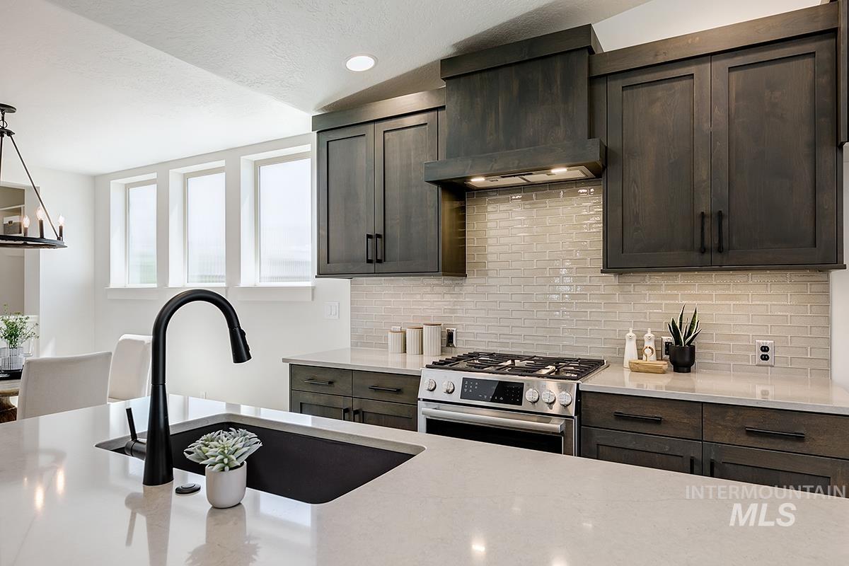 7151 South Skybreak Lane Meridian, ID 83642 - Photo 6 of 26 Kitchen featuring a large island with an undermount sink and matte black faucet, dark wood-finish cabinetry, stainless steel range, light-toned backsplash, and recessed lighting