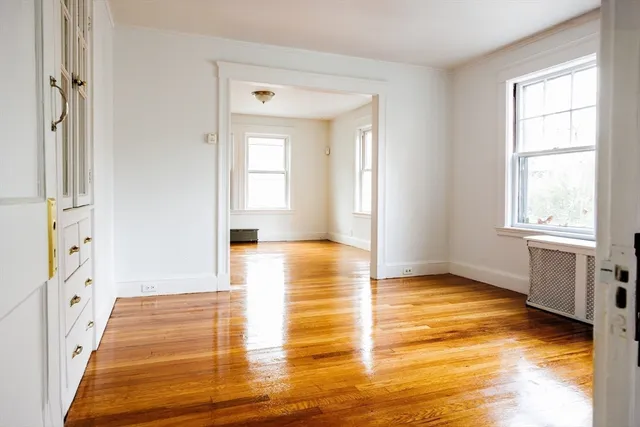 a view of an empty room with window and wooden floor