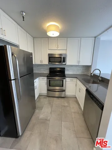 a kitchen with stainless steel appliances granite countertop a refrigerator a stove a sink and white cabinets