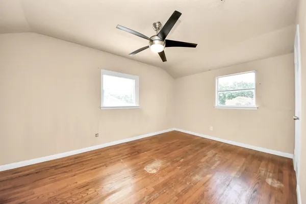 a view of an empty room with wooden floor and a ceiling fan