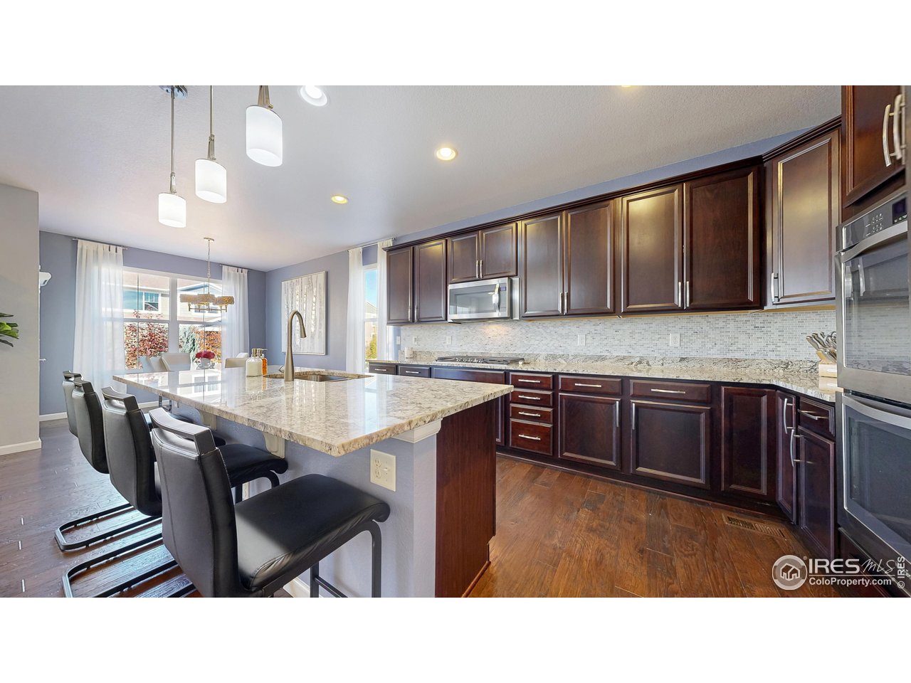 6794 Spring Rain Road Timnath, CO 80547 - Photo 10 of 49 a kitchen with stainless steel appliances kitchen island granite countertop a table chairs sink and cabinets