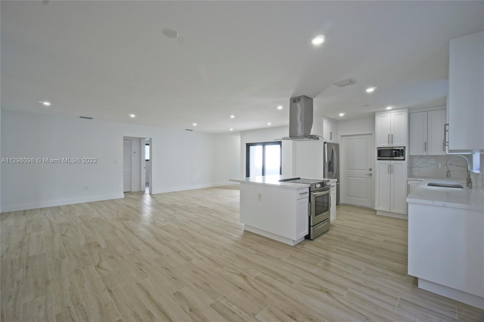 434 Southwest 23rd Road Miami, FL 33129 - Photo 3 of 32 a large white kitchen with kitchen island a sink wooden floor and a refrigerator