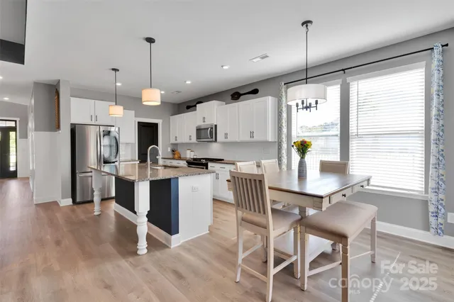 a kitchen with stainless steel appliances kitchen island granite countertop a table chairs and a wooden floor