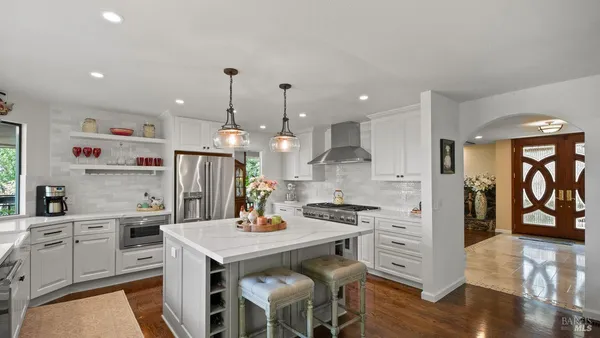 a kitchen with stainless steel appliances kitchen island granite countertop a refrigerator a stove and white cabinets with wooden floor