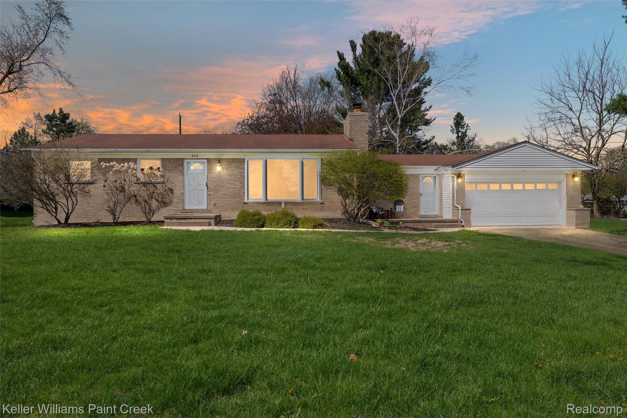Ranch-style home with driveway, an attached garage, a front lawn, brick siding, and entry steps