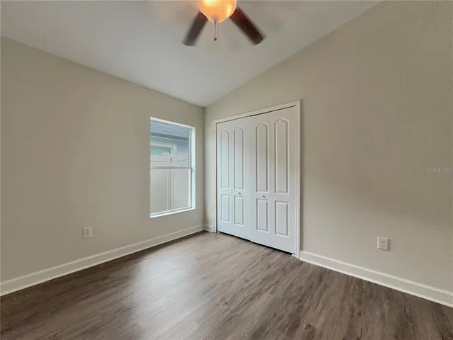 an empty room with wooden floor chandelier fan and windows